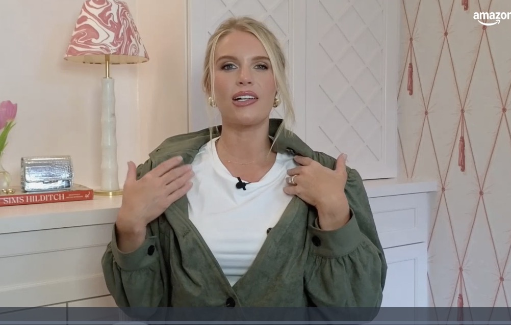 A blonde woman in a white t-shirt and green jacket speaking to the camera.